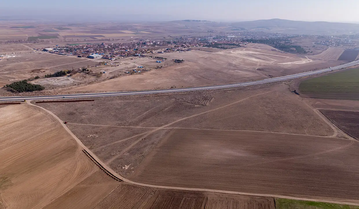 Arazinin drone ile çekilmiş genel görünümü — önde düz arazi, ortada Konya yolu, arkada Mahmudiye yerleşimi